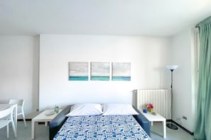 A hotel room with a bed, a desk, a chair, and a floor lamp. - Apartment on the beach facing Lake Como. Air conditioning, wifi, internal parking and beach access are free!The house is located right in front of the lake, from where you can enjoy the beautiful view of the lake. Bellano center and Bellano Tartavalle Te (Bellano)