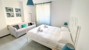 A bedroom with a white bed, a white sofa, and a blue lamp. - Apartment on the beach facing Lake Como. Air conditioning, wifi, internal parking and beach access are free!The house is located right in front of the lake, from where you can enjoy the beautiful view of the lake. Bellano center and Bellano Tartavalle Te (Bellano)