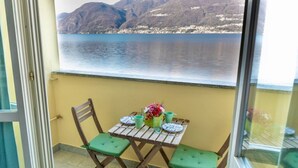 A balcony with a table and chairs, a view of a lake and mountains, and a glass door. - Apartment on the beach facing Lake Como. Air conditioning, wifi, internal parking and beach access are free!The house is located right in front of the lake, from where you can enjoy the beautiful view of the lake. Bellano center and Bellano Tartavalle Te (Bellano)