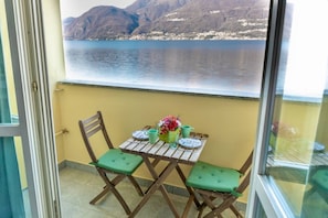 Un balcone con tavolo e sedie, vista su un lago e montagne, e una porta in vetro.