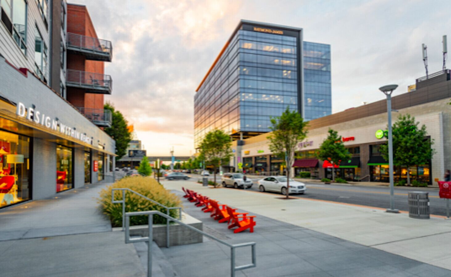 A modern urban street with commercial buildings, a clear sky, and a pedestrian walkway.