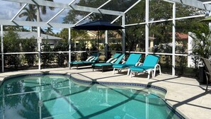 A pool area with a glass enclosure, lounge chairs, and a tiled pool edge. - Perfect Fort Myers Getaway!  Close to beaches, downtown, nightlife.. (Fort Myers)
