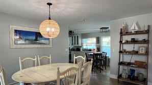 A dining area with a round table and chairs, a hanging light fixture, and a kitchen in the background. - Perfect Fort Myers Getaway!  Close to beaches, downtown, nightlife.. (Fort Myers)