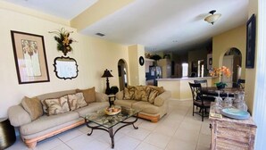 A living room with a sofa, coffee table, and a wooden cabinet with glassware. - Southern Dunes Golf Views! 5 Bedroom Home by RedAwning (Haines City)