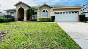 A two-story house with a garage, a well-maintained lawn, and a clear sky. - Southern Dunes Golf Views! 5 Bedroom Home by RedAwning (Haines City)