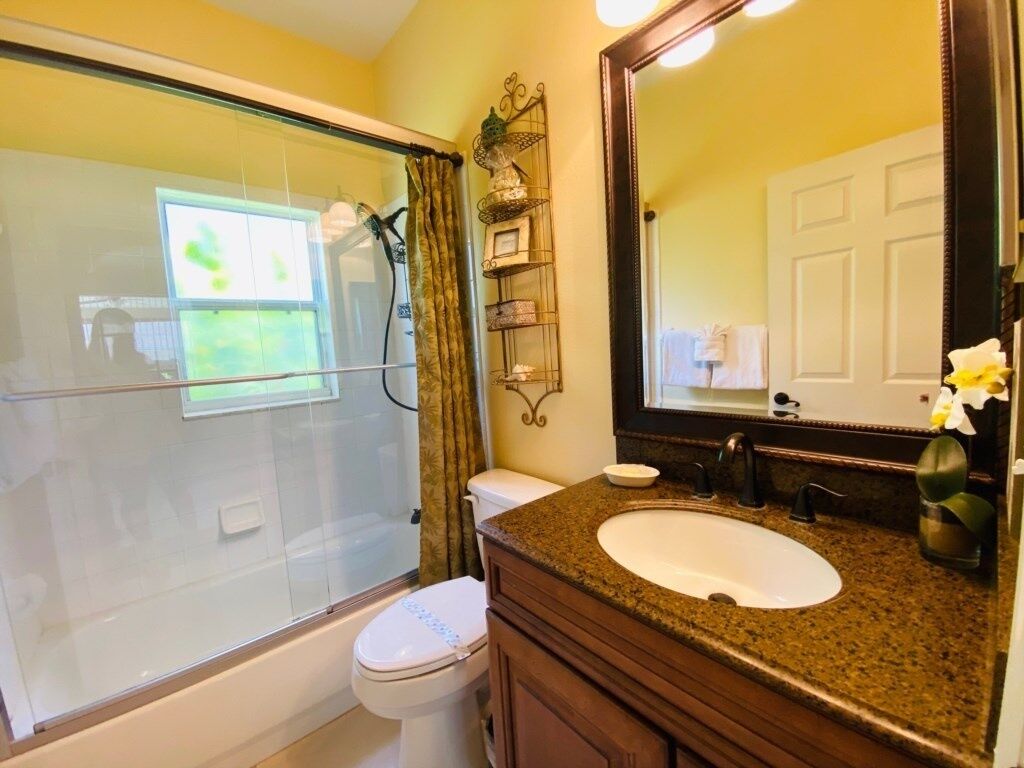 A bathroom with a glass shower enclosure, a white toilet, a granite countertop sink, and a large mirror.