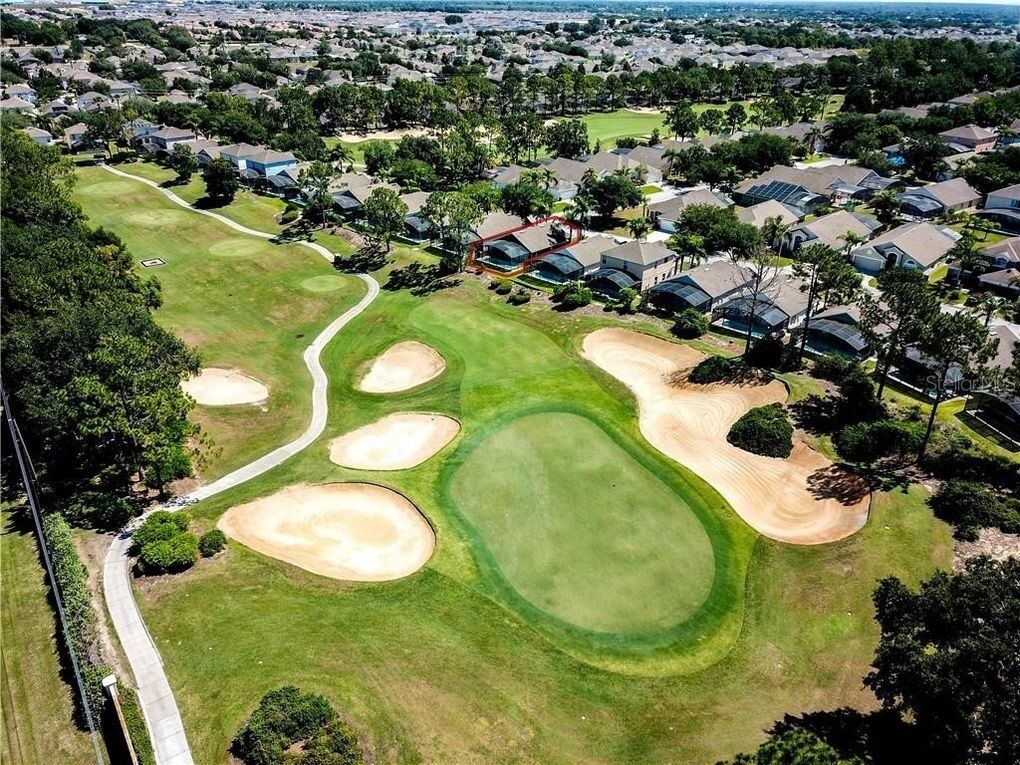 Vista aérea de un campo de golf con búnkeres de arena, un camino sinuoso y casas residenciales al fondo.