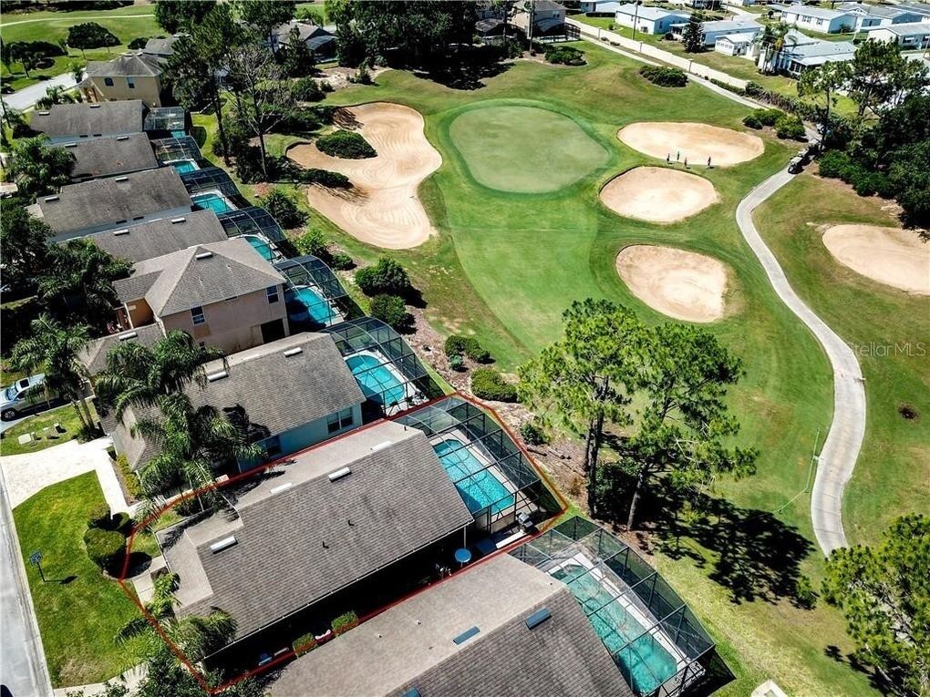An aerial view of a golf course with bunkers, a putting green, and a clubhouse with multiple swimming pools.