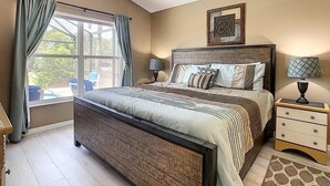 Une chambre à coucher avec un grand lit, deux tables de chevet, un ventilateur de plafond et une fenêtre avec des rideaux.