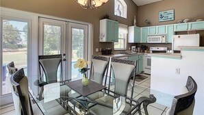 Une cuisine moderne avec des meubles de couleur turquoise, une table à manger en verre et un lustre.