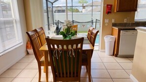 A dining area with a round table and six wooden chairs, a potted plant, and a view of a swimming pool through large windows. - Southern Dunes Golf With Views! 3 Bedroom Home by RedAwning (Haines City)