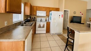A compact kitchen with wooden cabinets, a white stove, a refrigerator, and a microwave. - Southern Dunes Golf With Views! 3 Bedroom Home by RedAwning (Haines City)