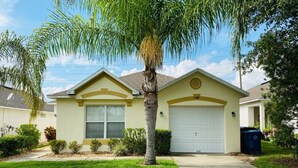 A single-story house with a front garage, a well-maintained lawn, and a palm tree. - Southern Dunes Golf With Views! 3 Bedroom Home by RedAwning (Haines City)
