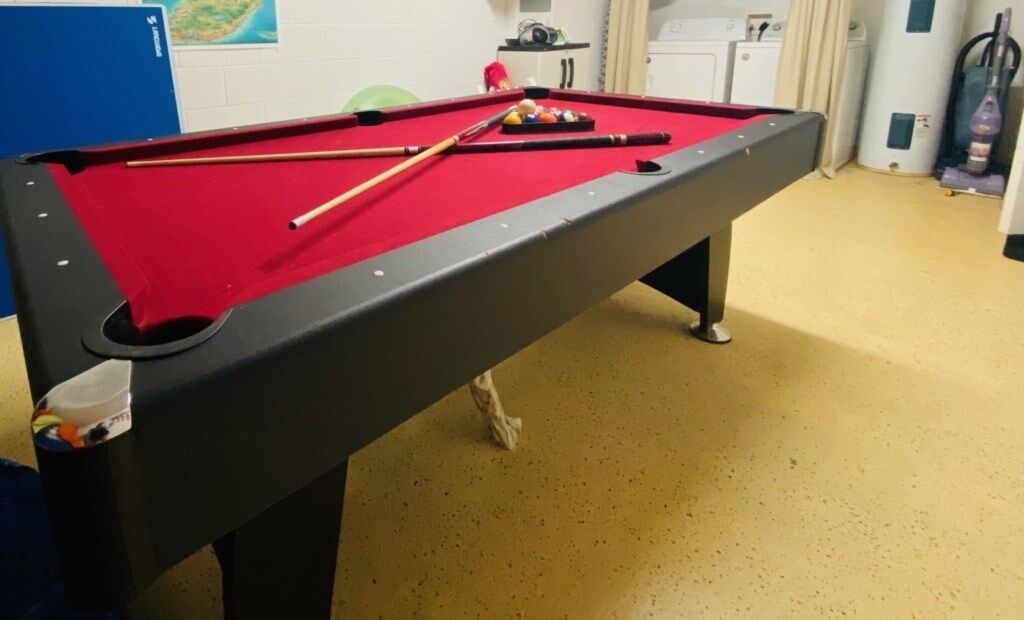 A pool table with a red felt surface, a cue stick, and billiard balls.
