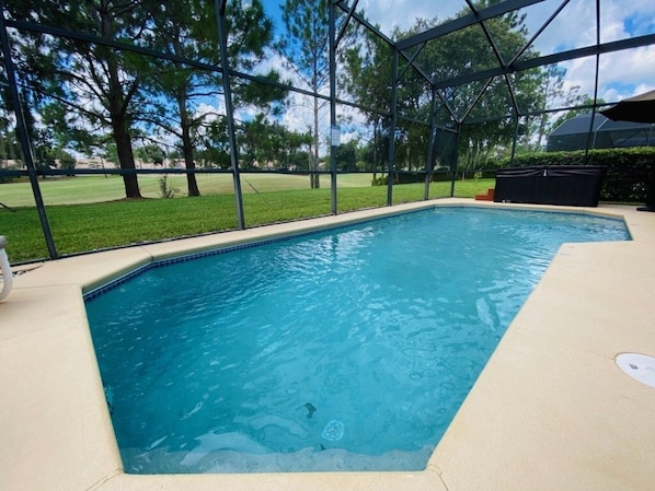 A rectangular swimming pool with clear blue water, surrounded by a beige deck and a metal safety fence.