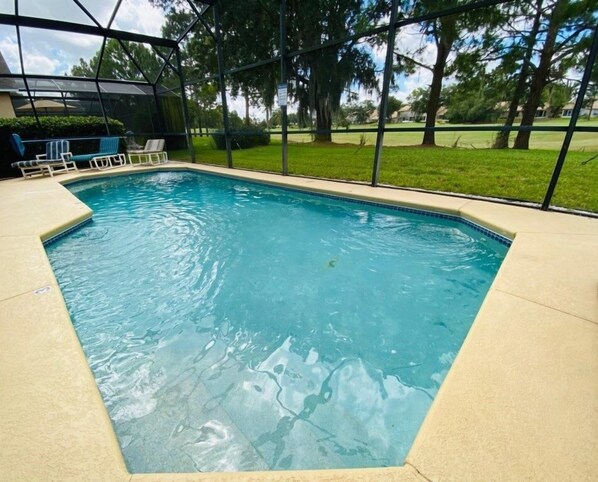 Una piscina rectangular con una superficie de agua azul cristalina, rodeada por un deck color beige y un cerramiento de vidrio.
