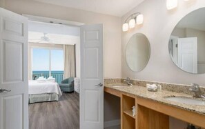 Habitación de hotel con una cama grande, un balcón con vistas, un lavabo doble y un espejo redondo.