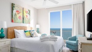 A hotel room with a bed, a desk, a chair, and a large window with a view of the sea.