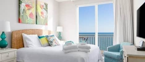 Een hotelkamer met een bed, een bureau, een stoel en een groot raam met uitzicht op zee.