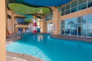 An indoor swimming pool with a colorful water slide, large windows, and a covered roof.