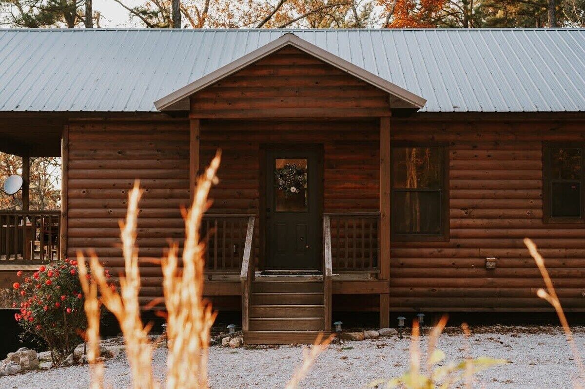 A wooden cabin with a front porch, a door with a wreath, and a gravel driveway.