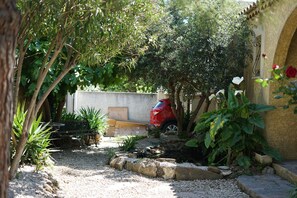 Un jardín con un sendero de grava, un coche rojo y un muro de piedra.