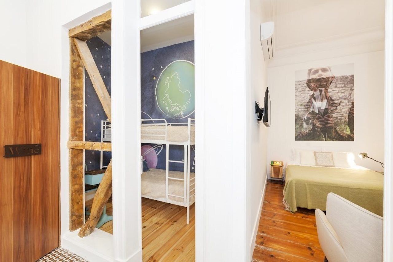 A room with a bunk bed, a bed, a wall with a painting, and a door with a wooden frame.