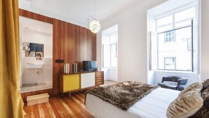 Un dormitorio moderno con piso de madera, una cama con manta suave, un televisor y un armario de madera.