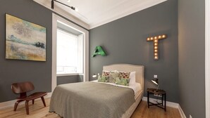 Un dormitorio con cama, una silla, una mesita de noche y una pared con letras iluminadas.