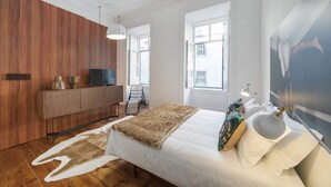 Un dormitorio moderno con un panel de madera en la pared, una cama con edredón blanco, una manta de piel y un ventanal con vistas a edificios.