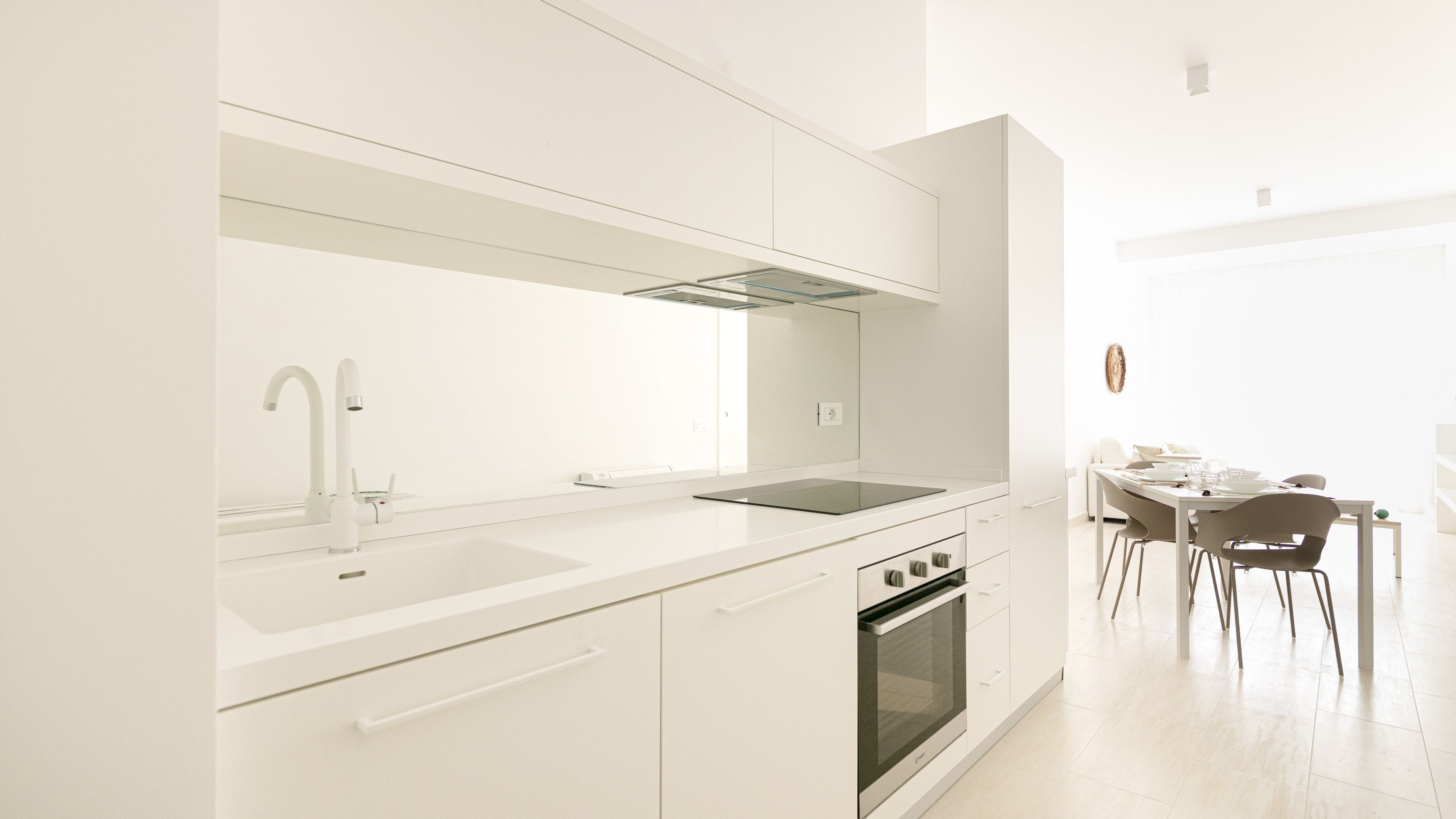 Una cucina moderna con mobili bianchi, forno integrato e zona pranzo con tavolo e sedie.