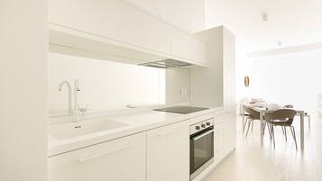 Una cucina moderna con mobili bianchi, forno integrato e zona pranzo con tavolo e sedie.