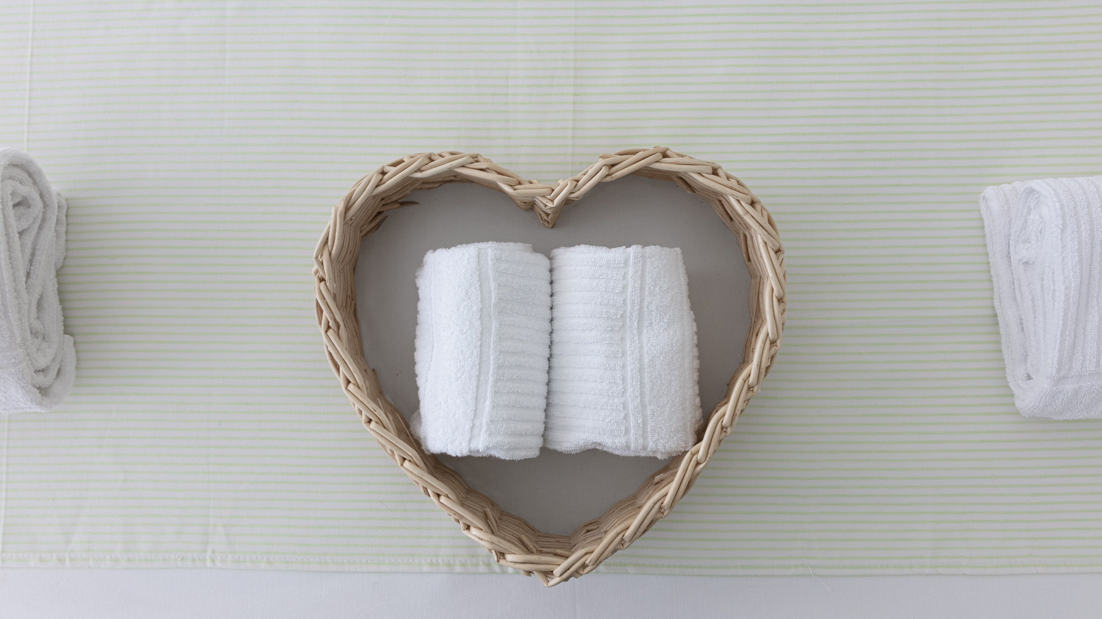 A heart-shaped wicker frame holding two white towels on a striped surface.
