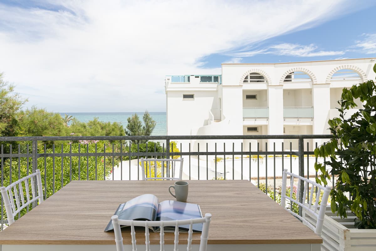 A wooden deck with a white chair and a mug, overlooking a sea view and a white building with arches.