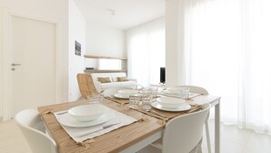 Un coin repas avec une table en bois dressée pour quatre personnes, des chaises blanches et un canapé blanc en arrière-plan.