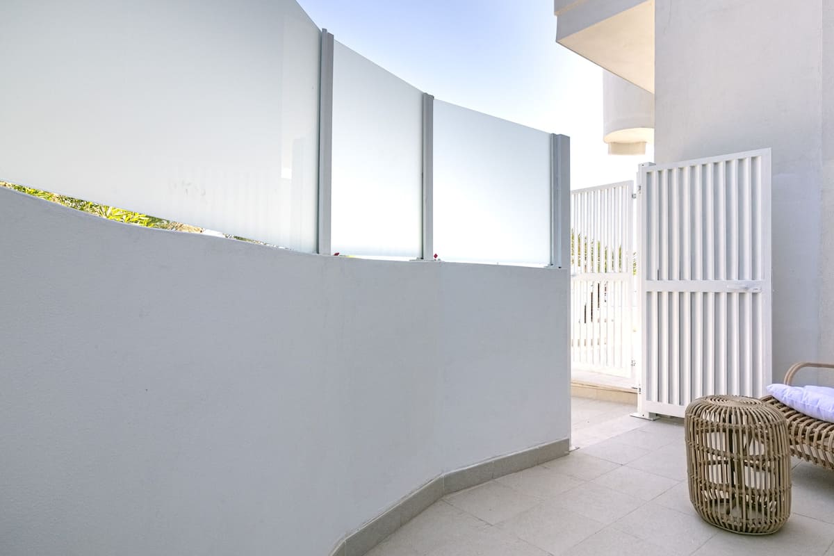 A balcony with a white wall, a wicker chair with a cushion, and a white gate.
