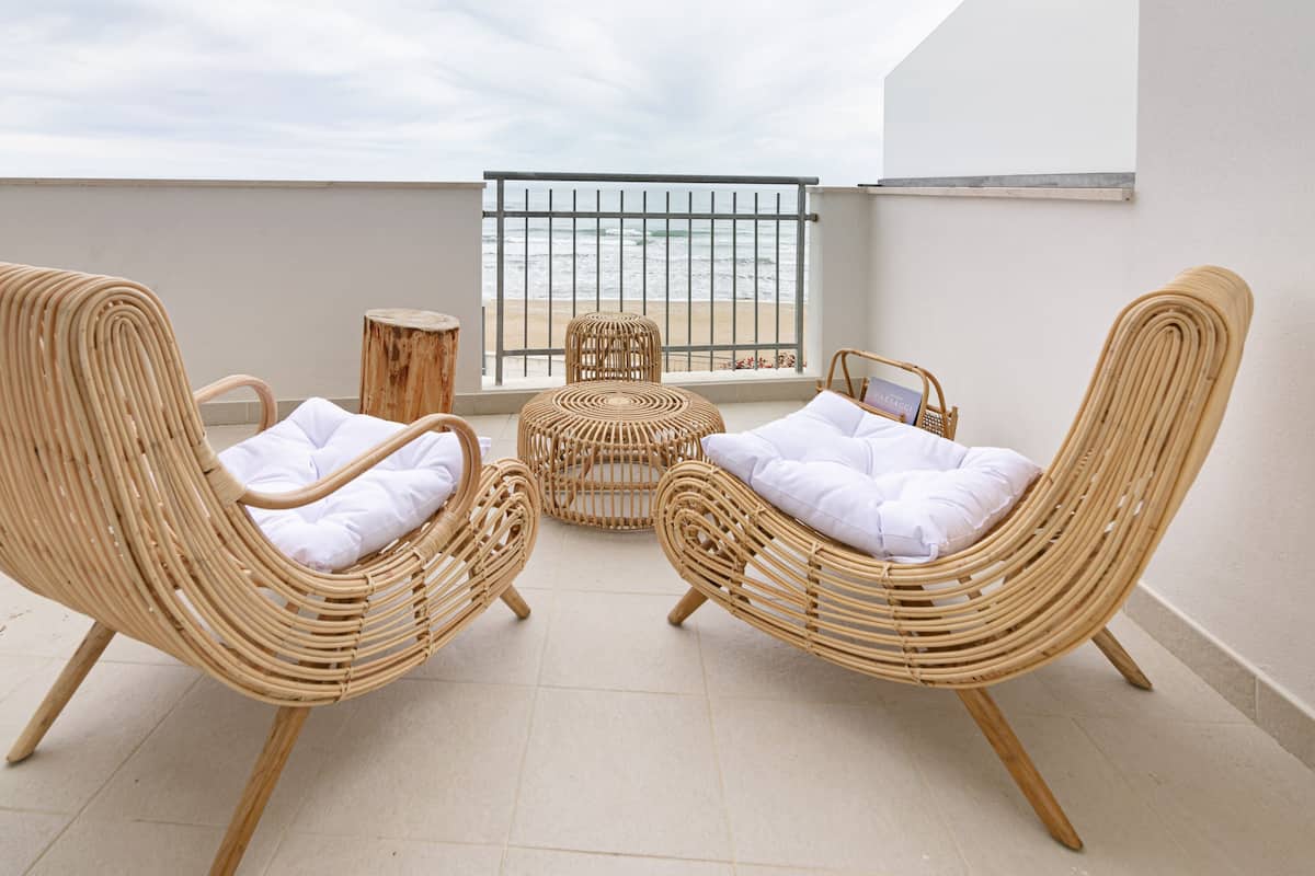 A balcony with two wicker chairs and a small round table, a wooden stool, and a metal gate.