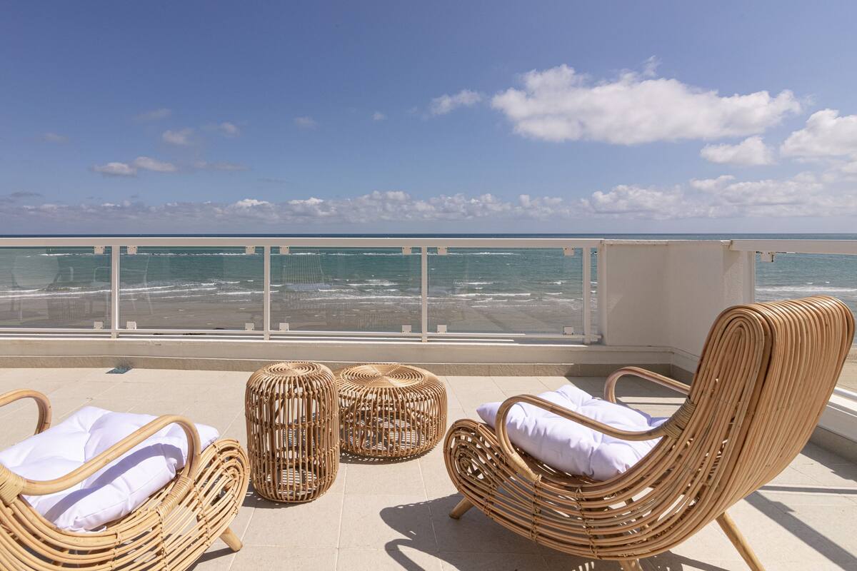 A balcony with wicker furniture and a view of the beach.