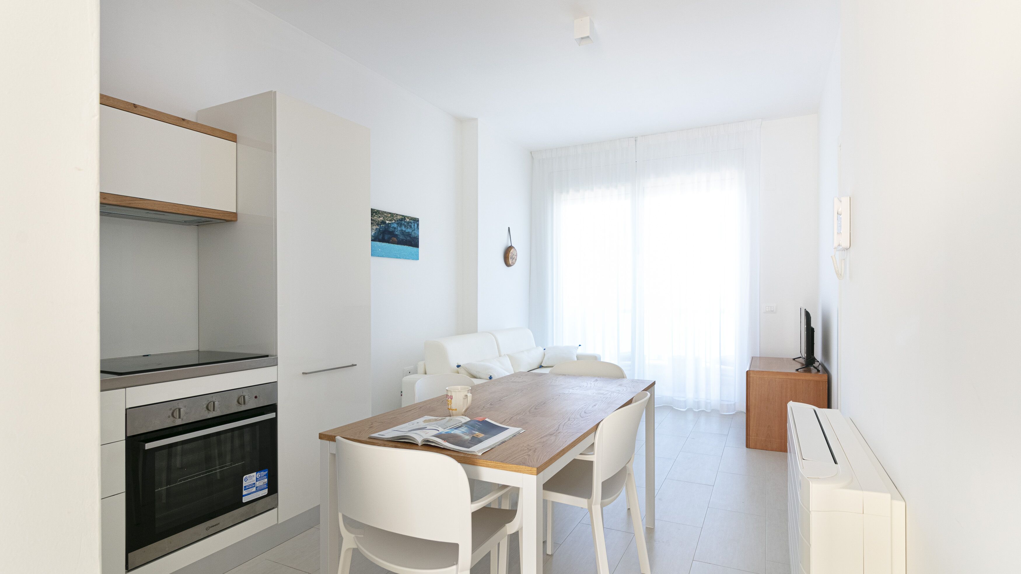 A modern kitchen with a built-in oven and a dining area with a wooden table and white chairs.