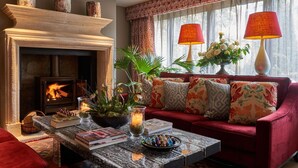 A cozy living room with a fireplace, a sofa with patterned cushions, a coffee table with books and decorative items, and two lamps on a side table. - Oppulent Lansdown Crescent Mews House with Free parking - Pass the Keys (Bath)