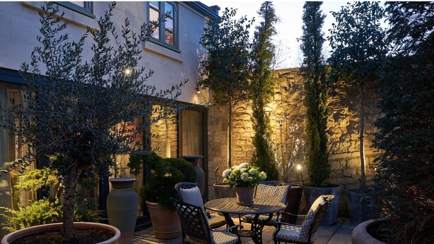 An outdoor patio with a round table and chairs, surrounded by potted plants and a stone wall. - Oppulent Lansdown Crescent Mews House with Free parking - Pass the Keys (Bath)