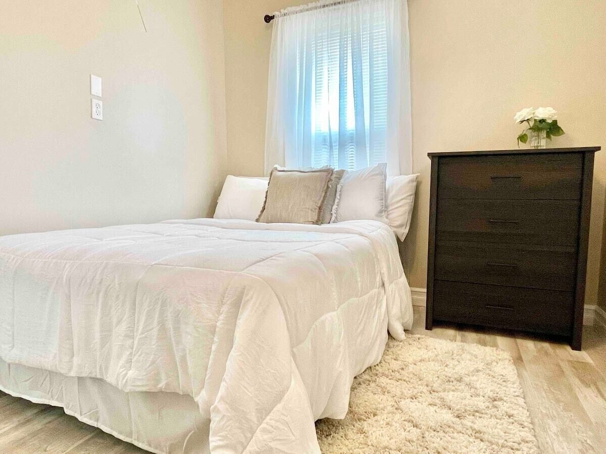 A bedroom with a bed, a dresser, and a window with curtains.