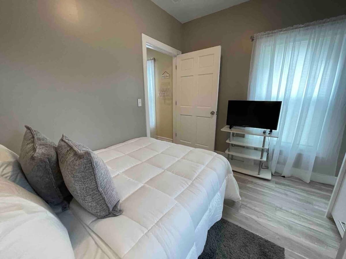 Un dormitorio con cama, almohadas, televisor y puerta.