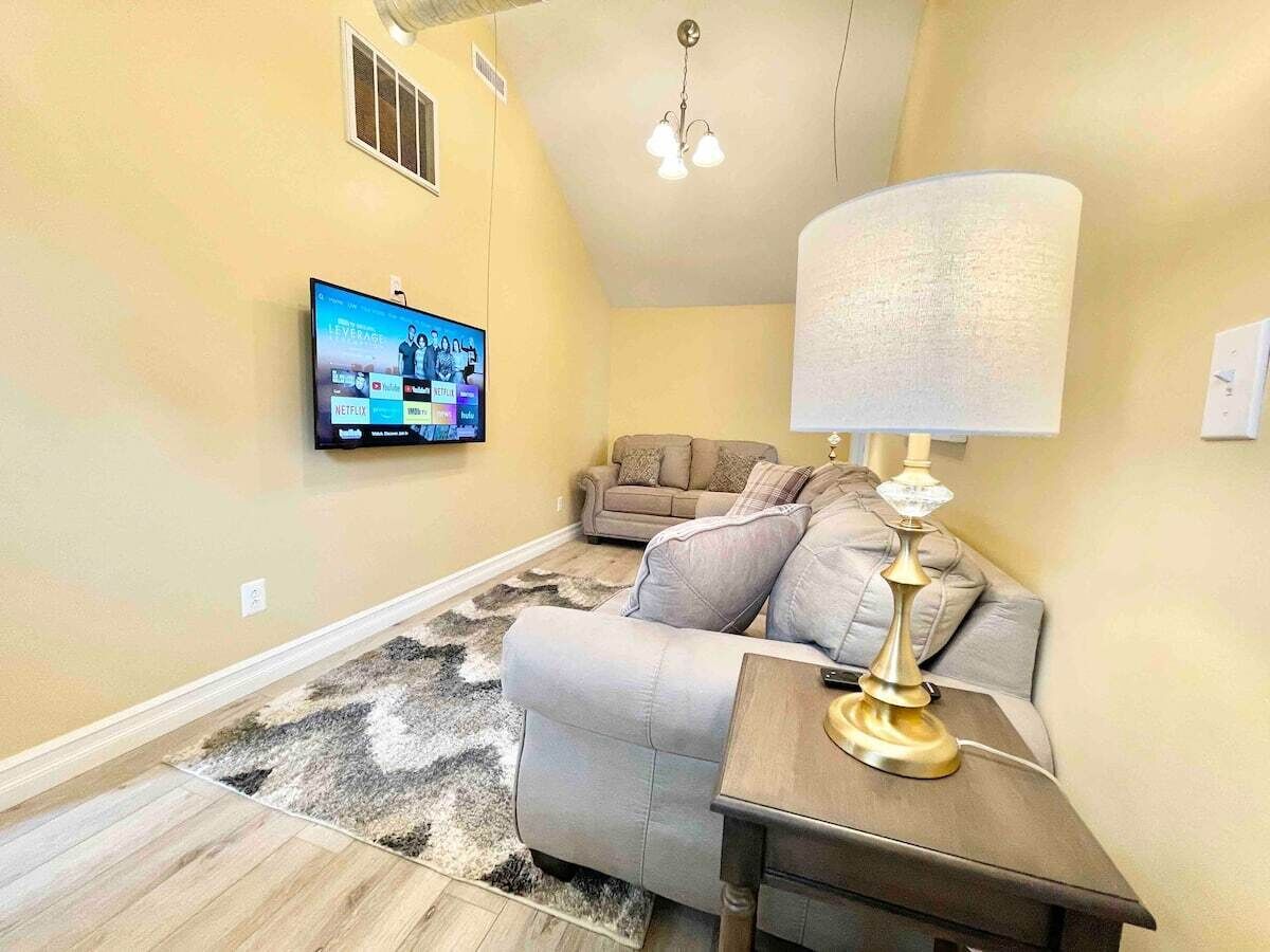 A living room with a sofa, a lamp, a TV mounted on the wall, and a patterned rug.
