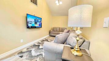 A living room with a sofa, a lamp, a TV mounted on the wall, and a patterned rug.