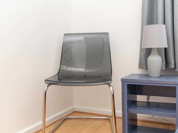 A modern chair with a transparent backrest and metal legs, positioned next to a small table with a white lamp. - Bright modern one bed apartment - Bath city centre - Pass the Keys (Bath)