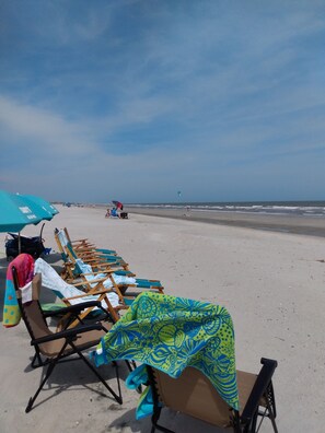 A beach with rows of sun loungers and umbrellas, a clear sky, and the ocean in the background.