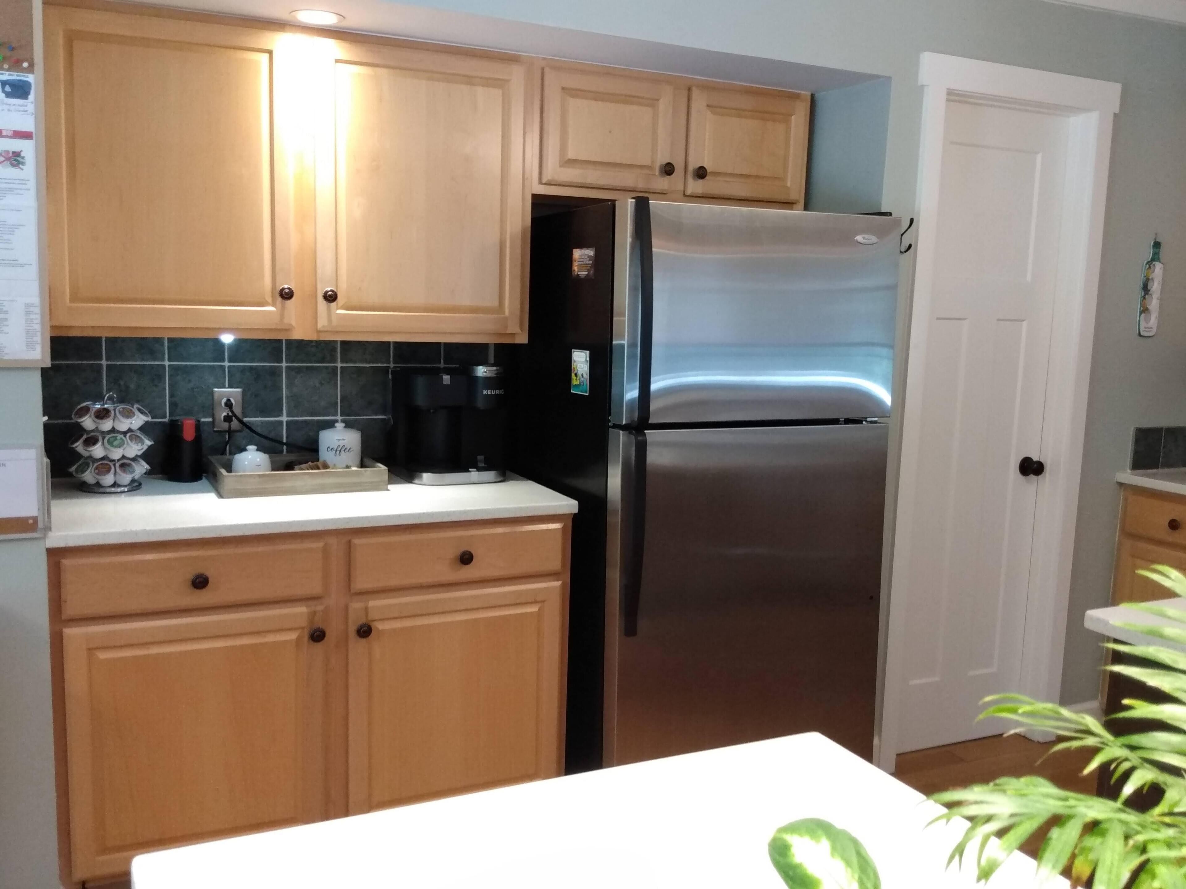 A kitchen with wooden cabinets, a stainless steel refrigerator, a coffee maker, and a white door.