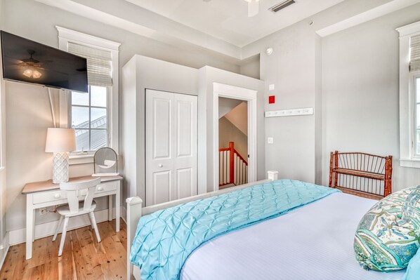 A bedroom with a bed, a desk, a chair, a TV, and a staircase.