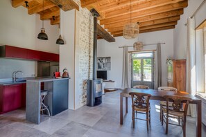 A modern kitchen with a central island, a dining area with wooden chairs, and a stone wall. - Maisonette with beautiful view (Cluny)